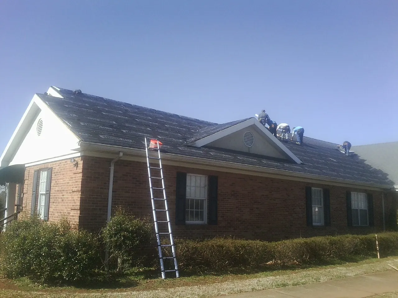 Crew tearing shingles off a brick ranch roof with a ladder set — Metal Roof Repair work by our crew in Fruitland